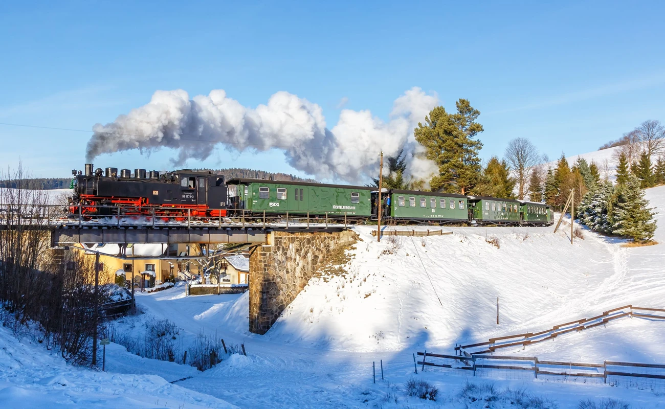 Sehmatal, Germany - December 18, 2022: Fichtelbergbahn steam train locomotive railway on a bridge in winter in Sehmatal, Germany.
