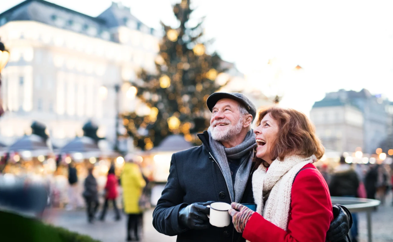 Happy senior couple on an outdoor Christmas market, holding enameled cups. Winter time.