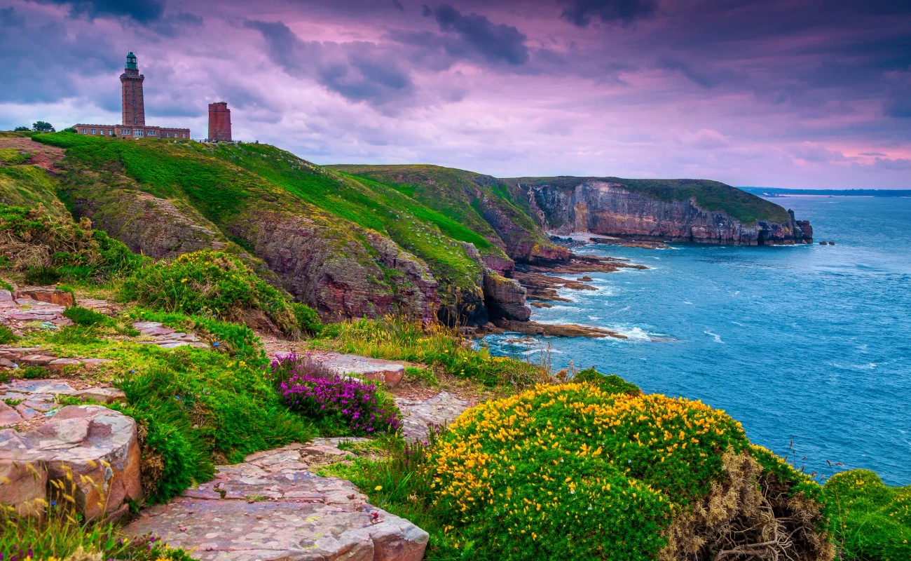 Spectacular lighthouse of Cap Frehel with flowery and rocky coastline at sunrise. Fantastic travel destination in Brittany, France, Europe