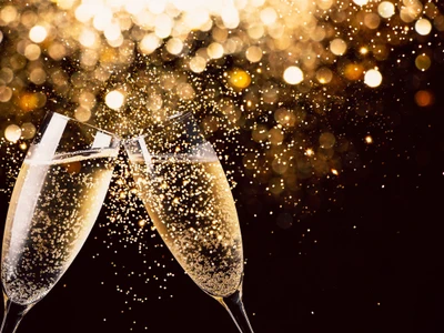 Two glasses of champagne toasting in the nigh with lights bokeh, glitter and sparks on the background