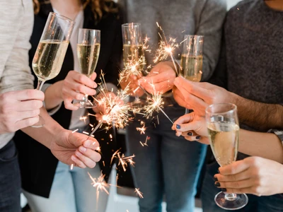 Group of happy friends holding flutes of sparkling champagne and burning bengal lights while enjoying party