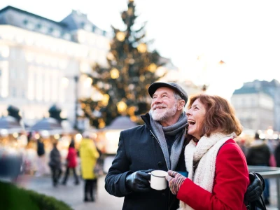 Happy senior couple on an outdoor Christmas market, holding enameled cups. Winter time.