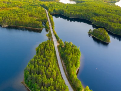 Aerial view of road between green summer forest and blue lake in Finland.