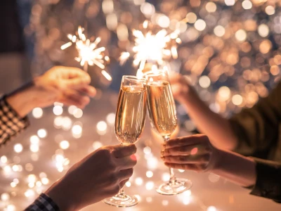 Hands of couple clinking with flutes of champagne and their friends holding sparkling bengal lights